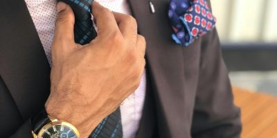 Elegant close-up of a man in a designer suit adjusting his tie, showcasing luxury fashion.